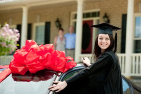 毕业生站在汽车旁边，上面有一个巨大的蝴蝶结。