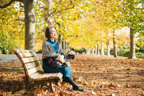 老女人在固定年金享受秋天的天气在公园的长椅上。