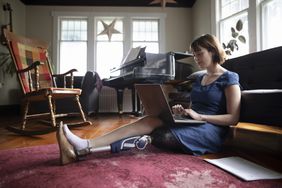 年轻女子截肢使用笔记本电脑在客厅的地板上