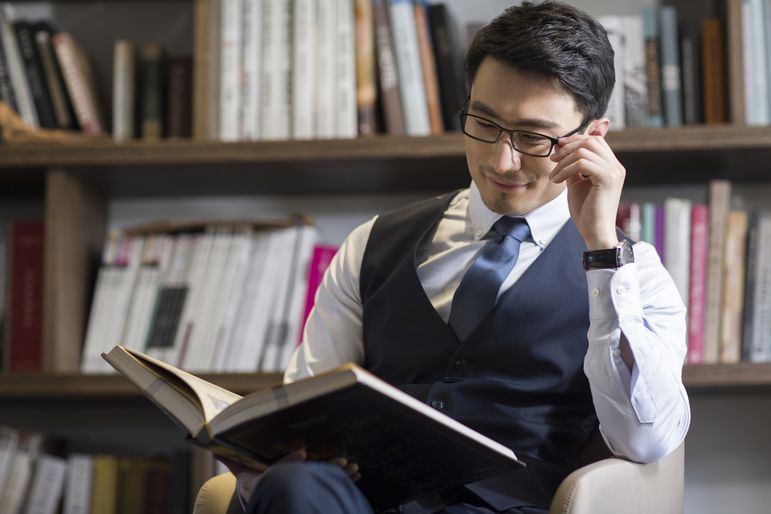戴眼镜的男人穿着正装衬衫、领带和背心在读一本书