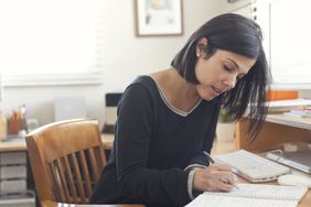 一个女人坐在办公桌前，在笔记本上列着清单。