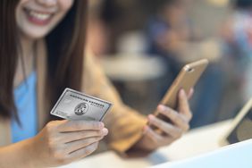 一名女子手持iPhone和美国运通商务白金卡。