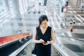 年轻的女商人在乘坐自动扶梯时用智能手机阅读电子邮件