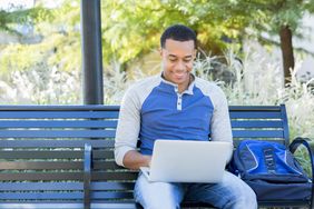一位面带微笑的投资者坐在公园的长椅上用笔记本电脑工作