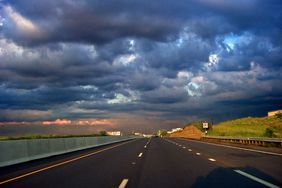 高速公路上的一辆汽车的影子，暴风雨云威胁着糟糕的驾驶条件