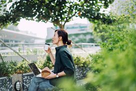 一个女人坐在公园里，用笔记本电脑工作，享受咖啡