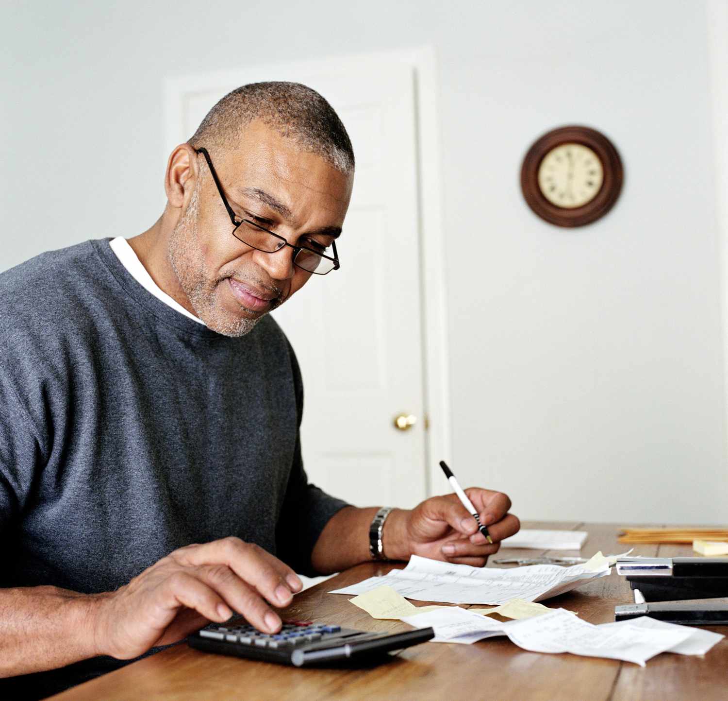 一名男子在家里用计算器计算平均每天的财务费用余额＂class=