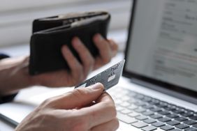 A hand holding credit card and wallet by laptop