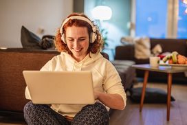 女人与笔记本电脑坐在大腿上戴着耳机”width=