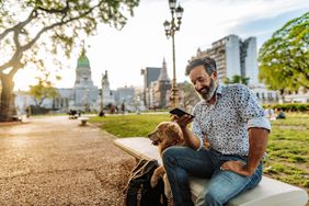 在阿根廷布宜诺斯艾利斯的春天，一个留着胡子、穿着时髦休闲服装的成熟男子在遛狗