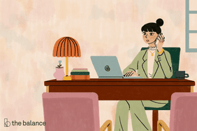 一个穿着西装的女人，坐在她的办公桌前，在打电话和笔记本电脑上