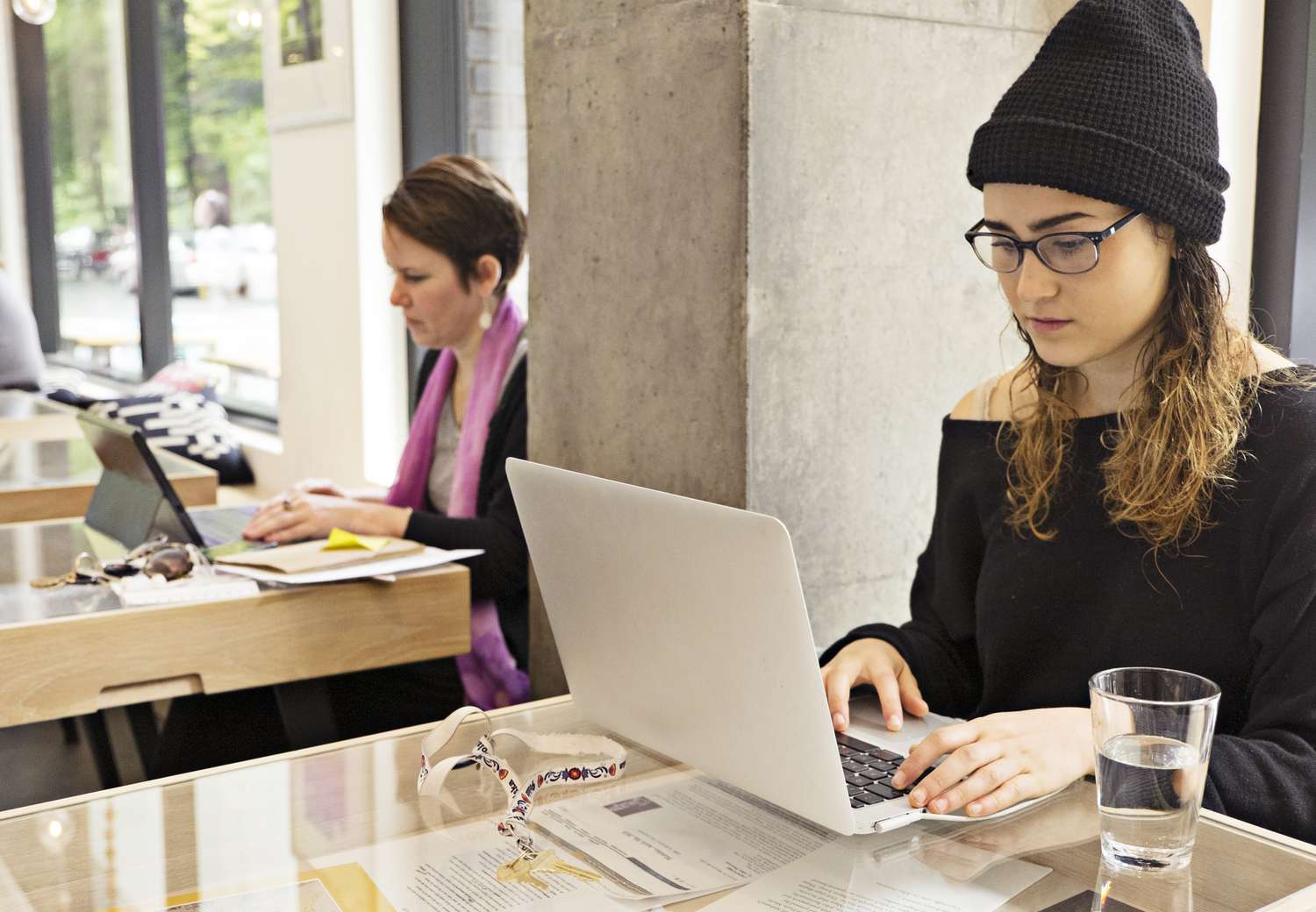 一个女人坐在咖啡馆里，手里拿着笔记本电脑和一杯水