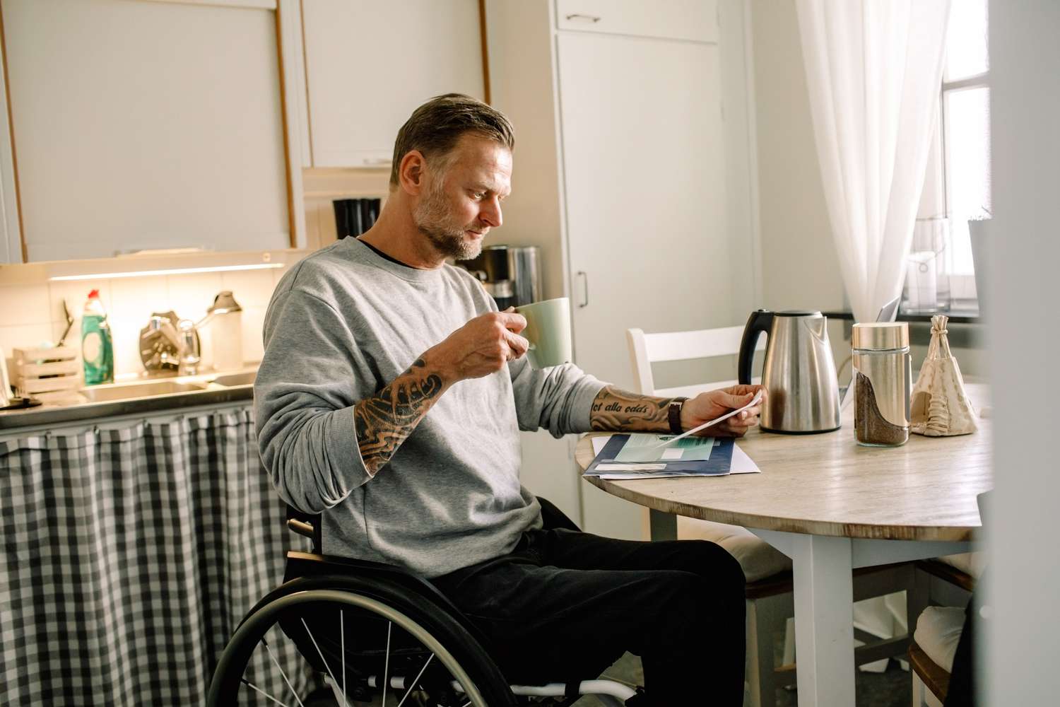 坐在轮椅上的男子在家里端着咖啡杯阅读邮件”class=