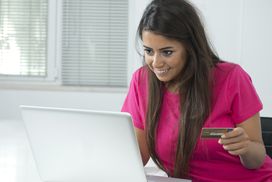 微笑的年轻女子网购信用卡和笔记本电脑。＂width=