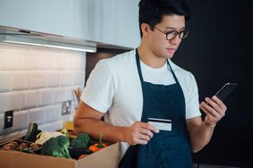 一个穿着围裙的男人拿着信用卡和电话。