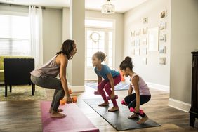 Mother doing yoga with daughters indoors.
