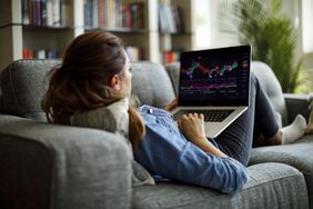 一个用笔记本电脑交易股票的女人躺在沙发上