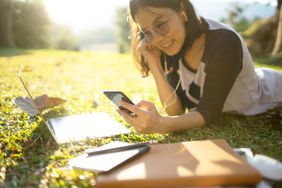 Student smiling while lying down on the grass listening to music from mobile phone