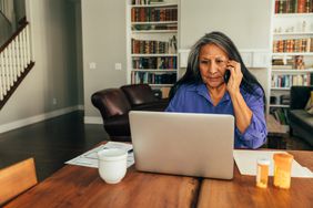 一个女人坐在她的餐桌与笔记本电脑付账单时,在电话里交谈