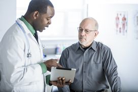 拿着数码平板电脑的医生在检查室与病人交谈”width=