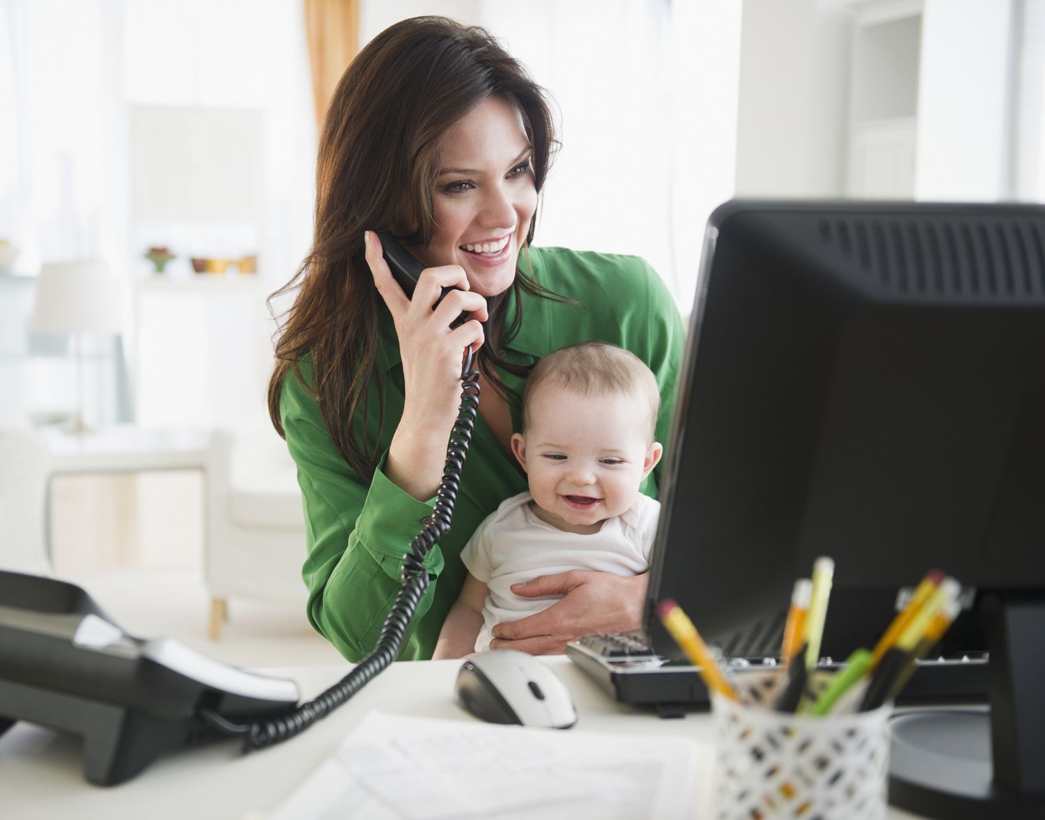 女人在电话和电脑上，在家工作时抱着孩子