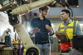 软件工程师向工厂焊工讲解控制机器人焊接过程。