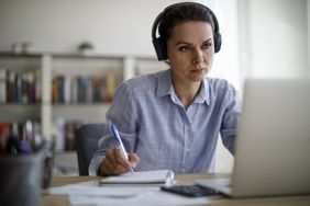 戴着耳机在电脑前记笔记的女人