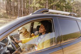 一位微笑的年轻女子驾驶着一辆车，副驾驶座位上坐着一只狗