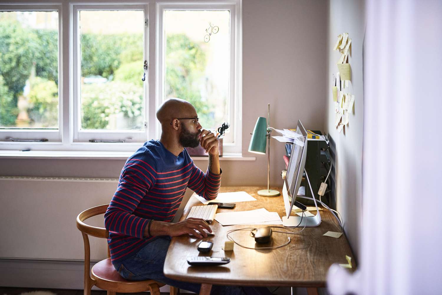 一个男人坐在办公室的台式电脑前，专注地看着屏幕，一只举起的手的一根手指按在他的嘴巴上，另一只手放在鼠标上