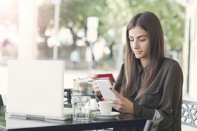 一位女士坐在咖啡桌旁思考她应该如何支付拿铁咖啡:信用卡还是信用卡?