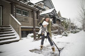 女人穿着一个婴儿童车,房子外铲雪