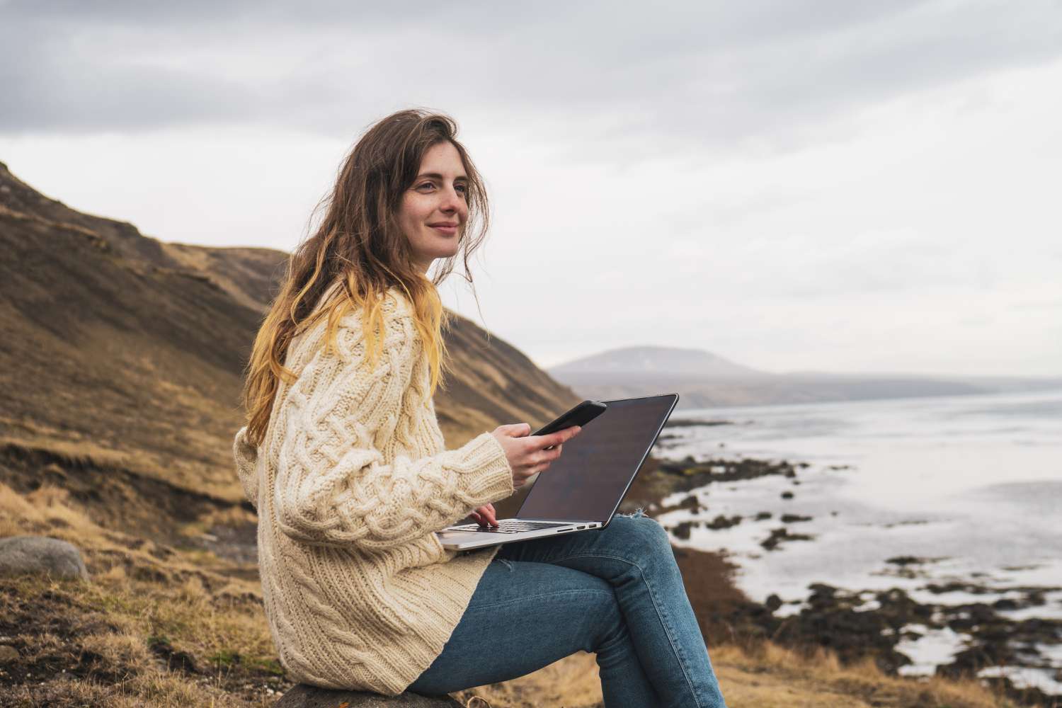 冰岛，一名女子在海边使用笔记本电脑和手机＂class=