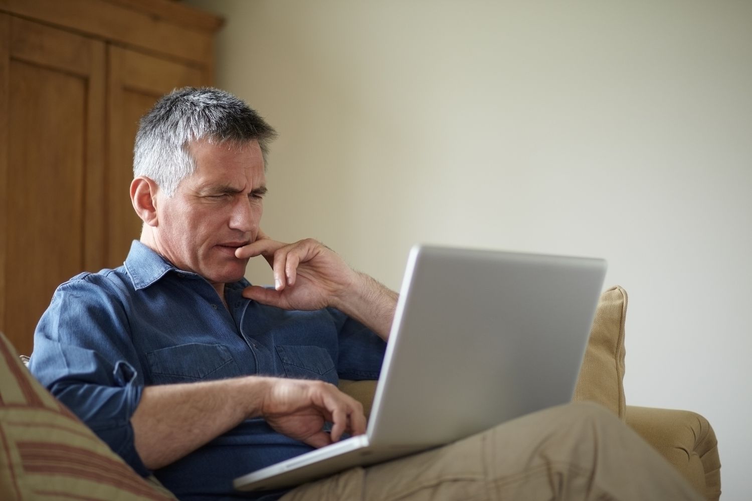 一个坐在沙发上的男人疑惑地看着膝上的笔记本电脑。