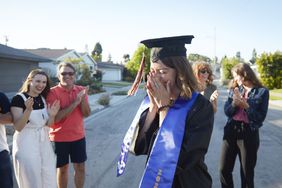 毕业的女人在黑色帽子和长袍和蓝色腰带遮住她的脸，而朋友们围在她外面