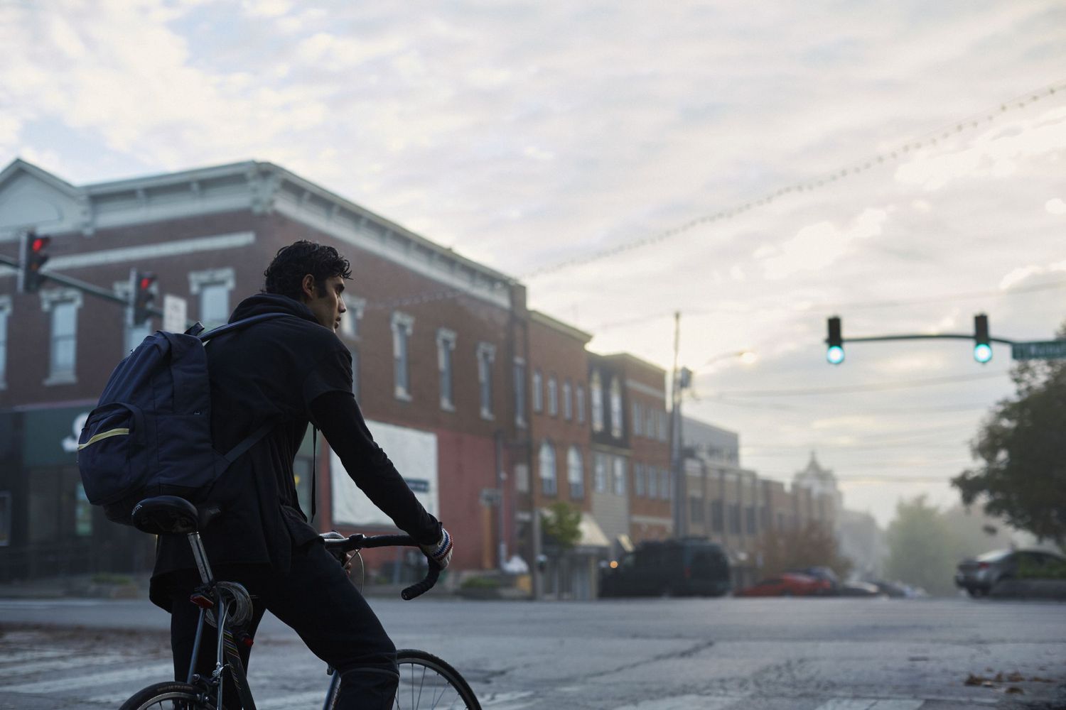 年轻人骑自行车与一个背包在小镇主要街道。”class=