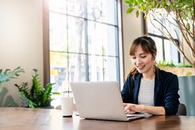 A person sits at desk with a laptop and a mug.