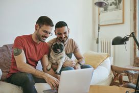 微笑的夫妇和哈巴狗在家里使用笔记本电脑