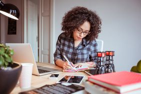 女自由职业者在家办公，在笔记本电脑前用笔记本写东西