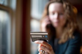 女人的手拿着信用卡，背景中她没有聚焦的图像，拿着手机”width=