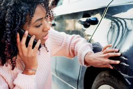女人检查她的车在电话上的划痕”width=