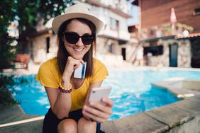 一个女人坐在树荫下一个闪闪发光的游泳池附近拿着信用卡和使用智能手机”>
          </noscript>
         </div>
        </div>
       </div>
       <div class=