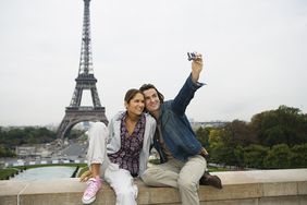 情侣坐在墙上，男子拍照，埃菲尔铁塔为背景