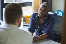 Physician with stethoscope listens intently to patient speaking