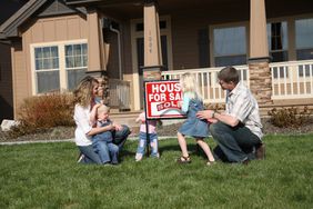 父母和三个年幼的孩子在他们家门前放置一个出售的标志