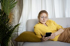 一名女子躺在沙发上看她的智能手机