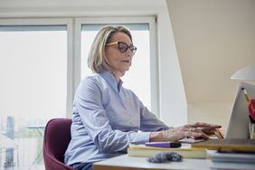 成熟的女人在家里使用笔记本电脑在办公桌上