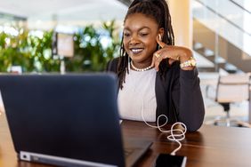 一个女人微笑着坐在桌子前，面前是一台打开的笔记本电脑