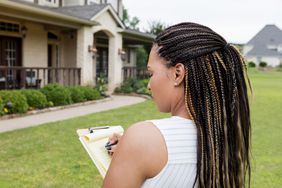 一个女人拿着写字板站在屋外，在写字板上写字