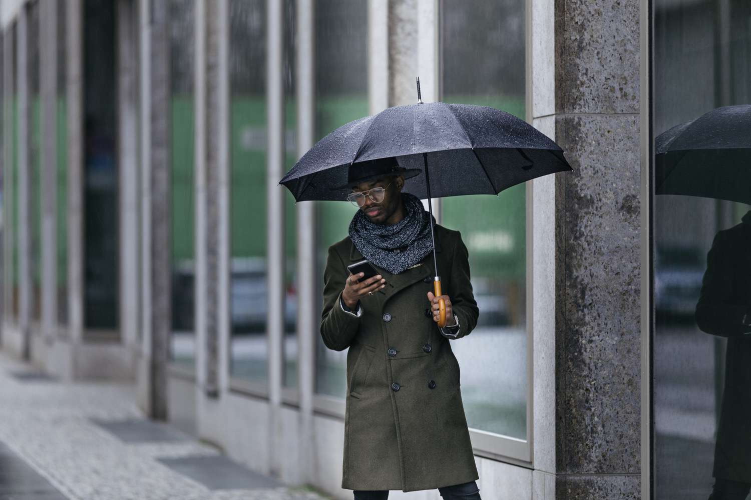 商人撑着伞，在雨中用智能手机发短信。