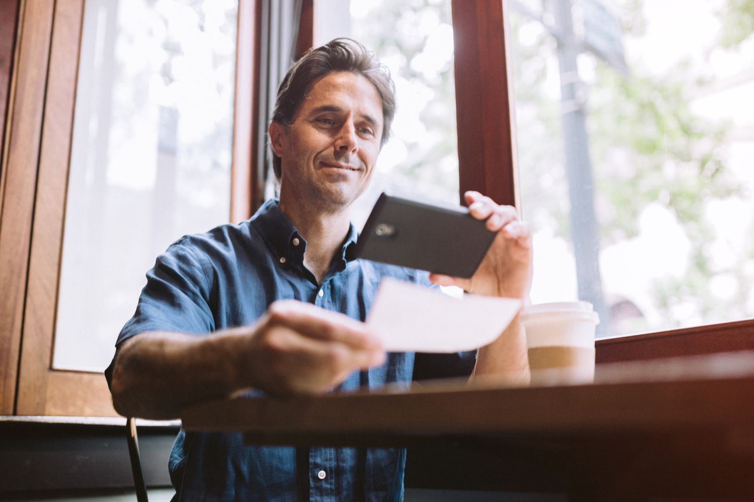 一名男子微笑着用他的智能手机拍摄支票或支票的数字电子存款
